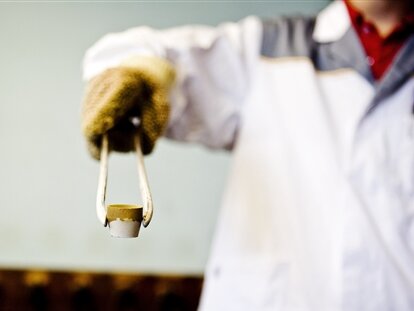 Ein Gold- und Silberschmied hält mit seiner Zange einen Behälter mitt Gold.