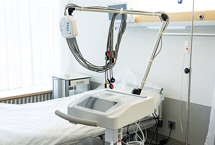 Ein EKG-Gerät steht vor einem Krankenhausbett.