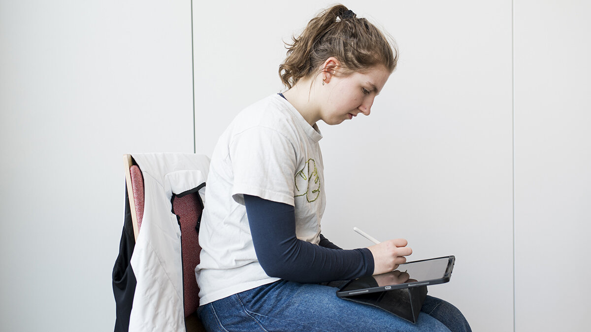 Liselotte sitzt im Klassenzimmer im Sportmanagement-Unterricht und arbeitet an einem Tablet.