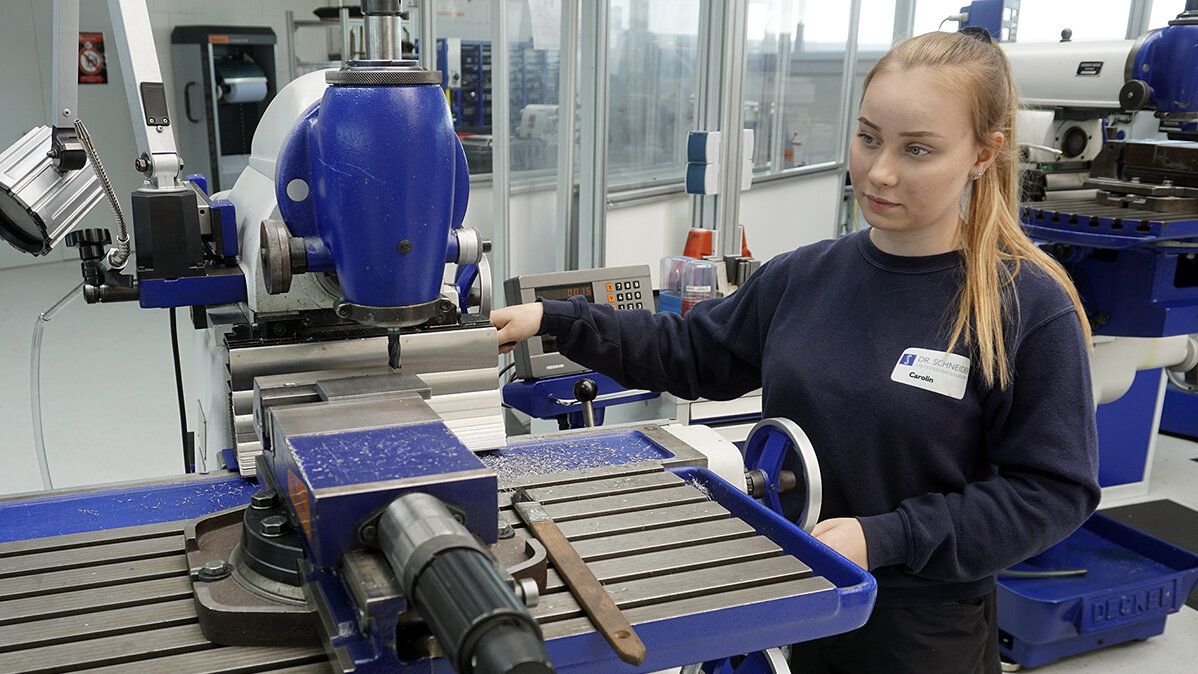 Eine junge Frau arbeitet mit einer CNC-Fräse.