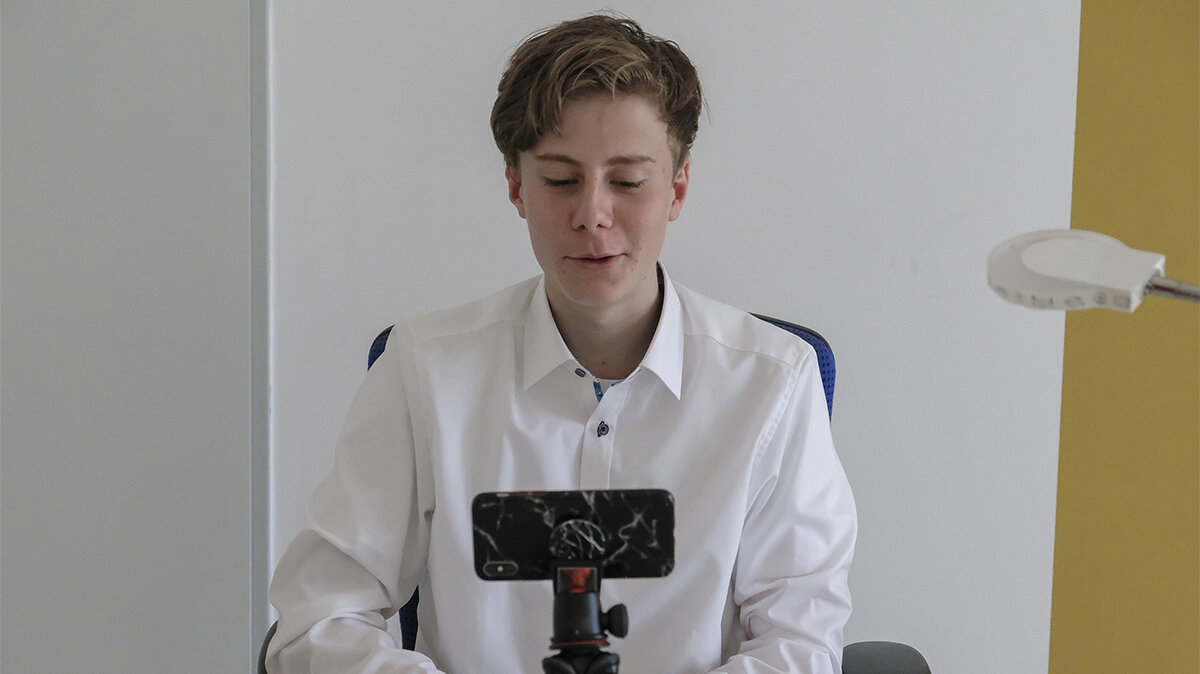 Ein junger Mann nimmt mit einem Handy auf einem Stativ ein Bewerbungsvideo auf.