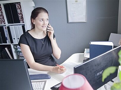 Eine junge Frau sitzt am Schreibtisch und telefoniert.