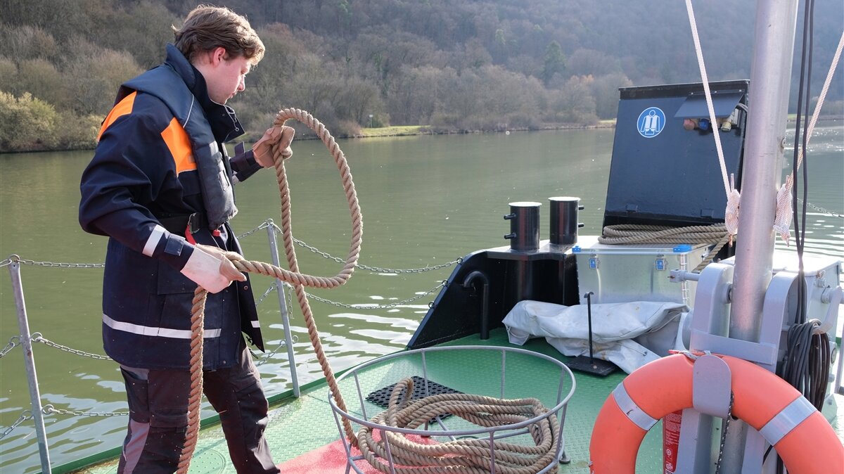 Ein Junger Mann legt ein Seil auf einem Boot zusammen. 