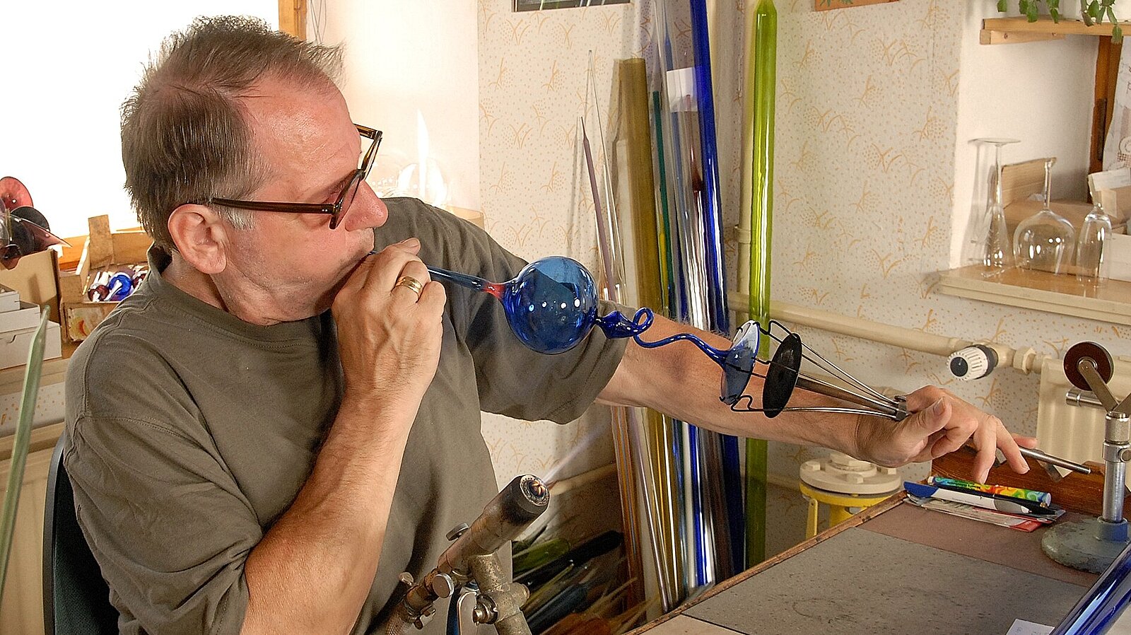Ein Mann formt Glas mit Glaspfeife und Flamme.