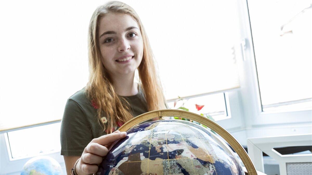Ein Mädchen zeigt auf einen Globus und schaut dabei in die Kamera.