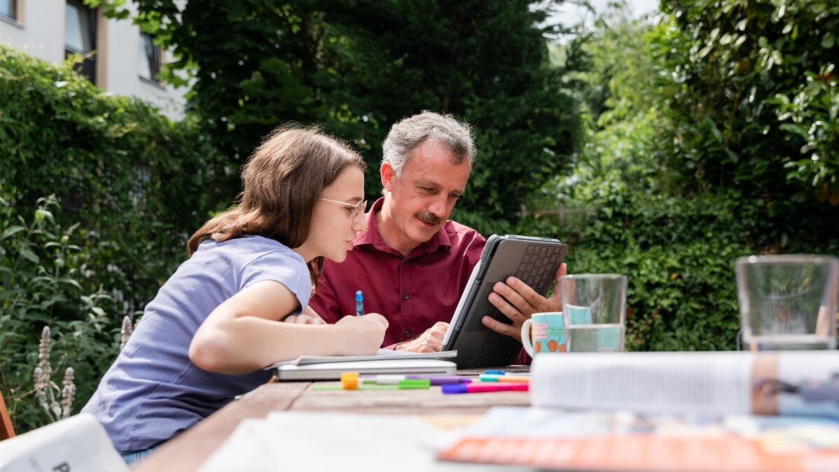 Ein Vater und seine Tochter sehen sich im Garten etwas auf dem Tablet an.