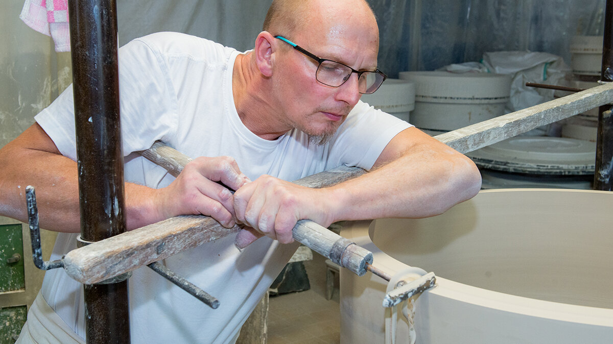 Ein Mann bearbeitet mithilfe eines Werkzeugs und Muskelkraft eine Keramik.