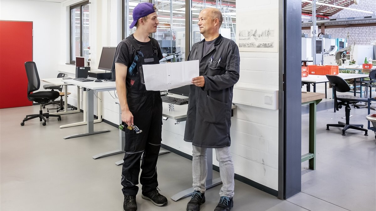 Luca und sein Ausbilder besprechen den Arbeitsauftrag mithilfe einer Zeichnung. 