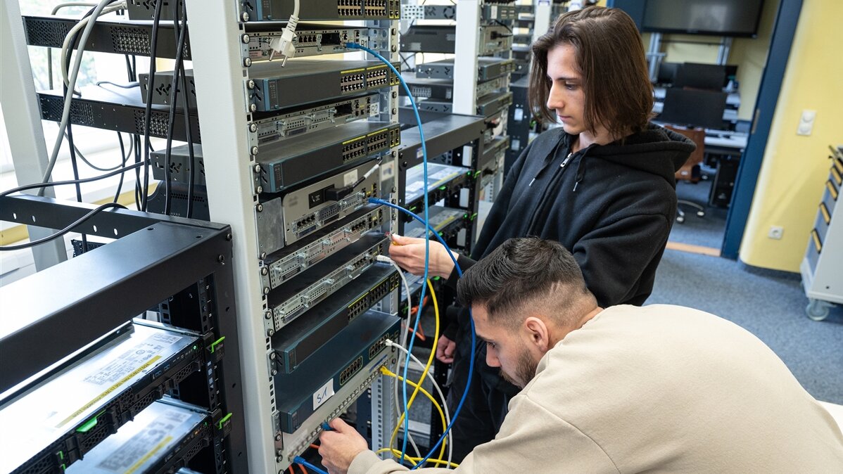 Zwei junge Männer in einem Serverraum stecken Kabel in einen Server ein.