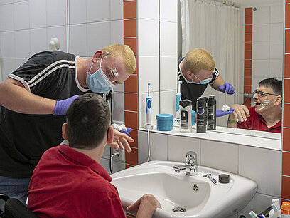 Ein junger Mann hilft einem Pflegebedürftigen bei der Rasur.