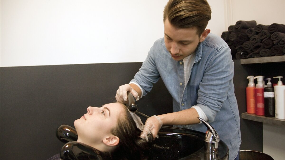 Ein junger Mann wäscht einer Frau im Friseursalon die Haare.