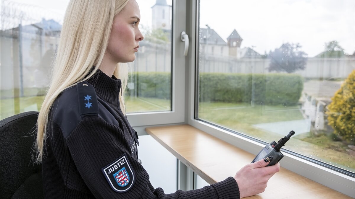 Lina sitzt an einem Tisch und hält ein Funkgerät in der Hand.