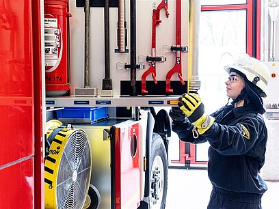 Eine junge Frau in Feuerwehruniform sucht im Feuerwehrauto nach einem Werkzeug.