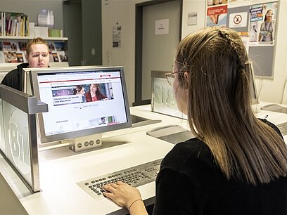 Eine junge Frau und ein junger Mann sitzen jeweils an einem Computer gegenüber.