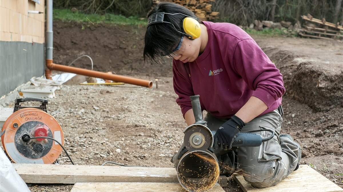 Hao schneidet vor dem Rohbau mit dem Winkelschneider ein Metallrohr. 