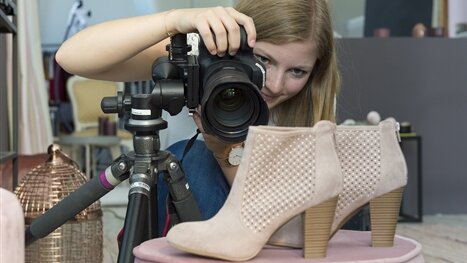 Eine junge Frau fotografiert mit einer großen Kamera ein Paar Damenschuhe.