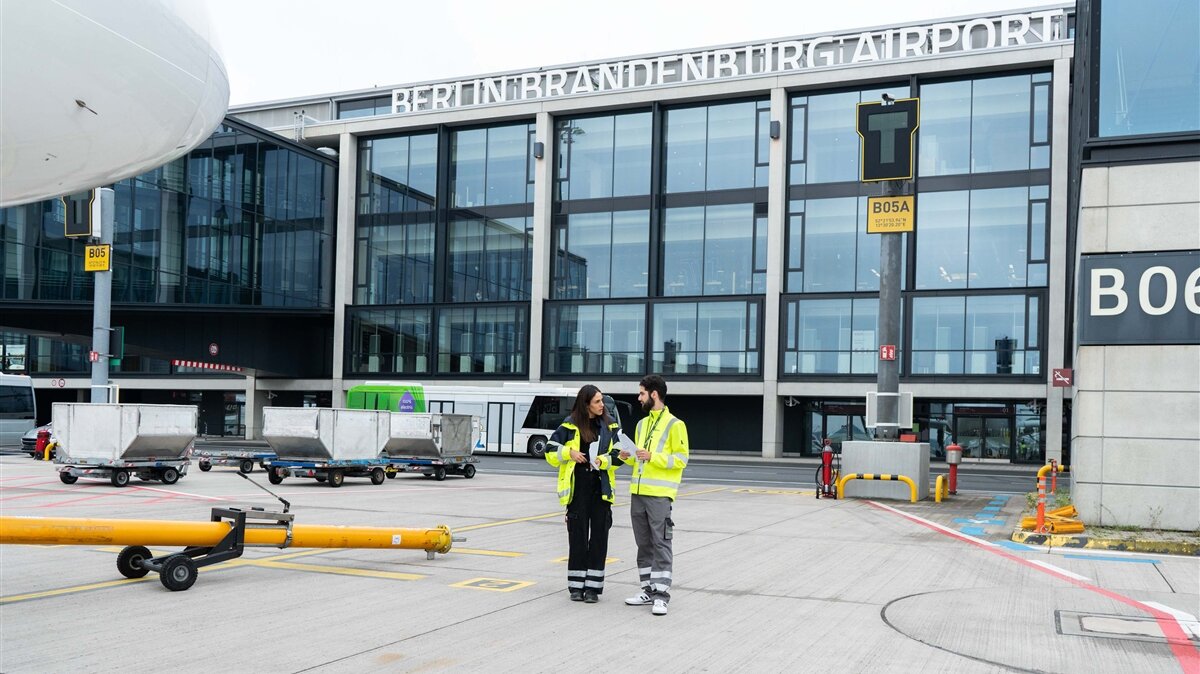Eine Frau und ein Mann stehen in gelben Warnwesten auf dem Rollfeld des Flughafen Berlin Brandenburg.
