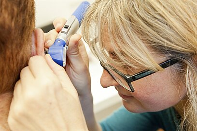 Eine Hörakustikerin sieht mit einem Gerät in das Ohr eines Patienten.