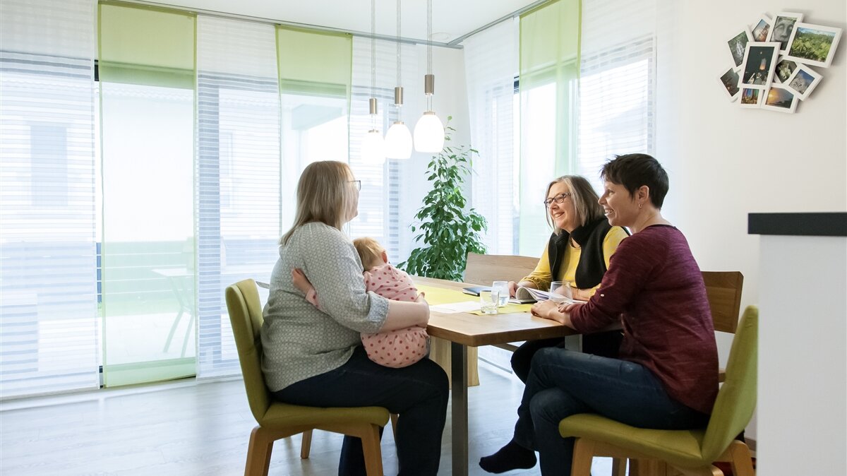 Drei Frauen und ein Kleinkind sitzen gemeinsam an einem Tisch.