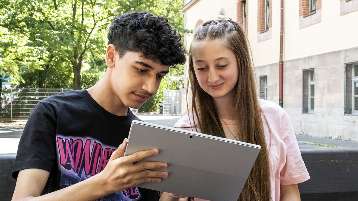 Ein Schüler zeigt einer Schülerin etwas auf einem Tablet.