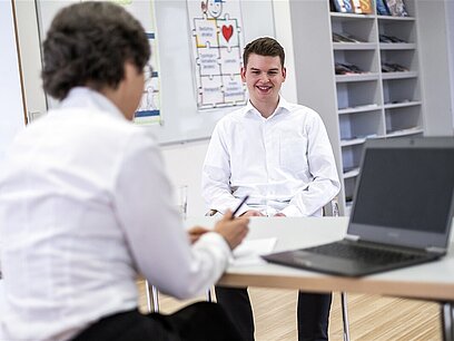 Eine Frau bittet eine junge Frau in einen Raum.