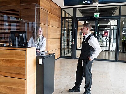 Eine junge Frau und ein junger Mann unterhalten sich an einem Serviceschalter.