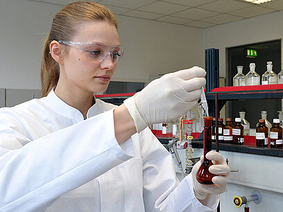 Eine junge Frau füllt im Labor mit einer Pipette eine Flüssigkeit in ein Reagenzglas.