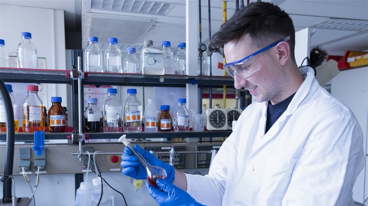 Ein junger Mann in Laborkleidung untersucht eine Abwasserprobe.