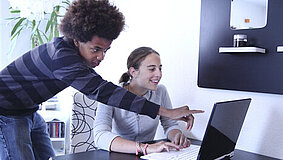 Ein Junge und ein Mädchen an einem Tisch schauen auf den Bildschirm eines Laptops.