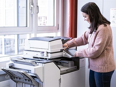 Eine junge Frau bedient in einem Büroraum einen großen Drucker.