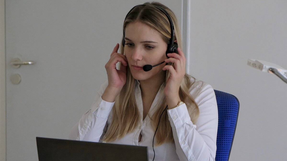 Eine junge Frau sitzt mit Headset am Computer.