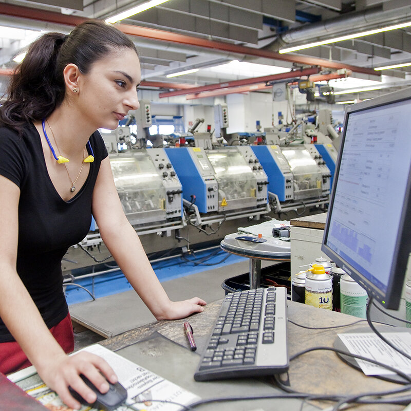 Eine junge Frau arbeitet an einem Computer in einer Fabrikhalle.