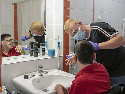 Ein junger Mann hilft einem älteren Mann beim Rasieren im Badezimmer. 