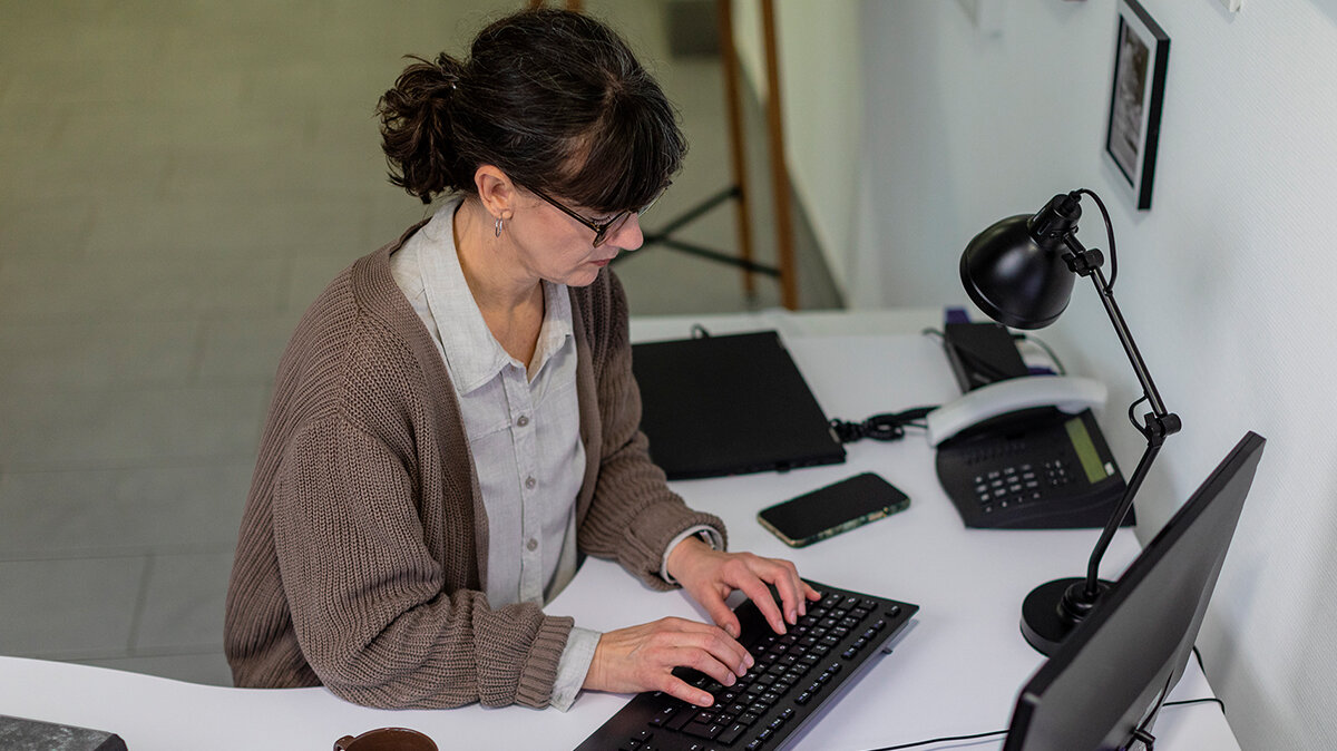 Eine Frau sitzt am Schreibtisch und tippt auf einer Computer-Tastatur.