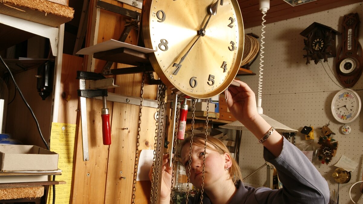 Eine Uhrmacherin repariert eine Wanduhr.