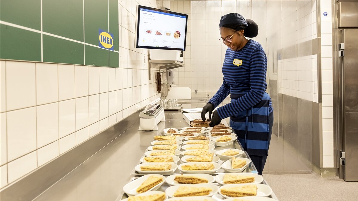 Josephat legt auf einer Arbeitsfläche in einer Großküche Kuchen auf Teller.
