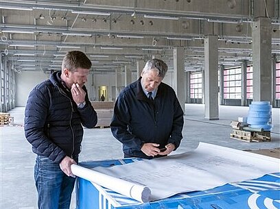 Zwei Männer stehen vor einem ausgerollten Bauplan.