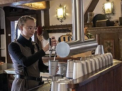 Eine junge Frau zapft am Zapfhahn an der Theke ein Bier.