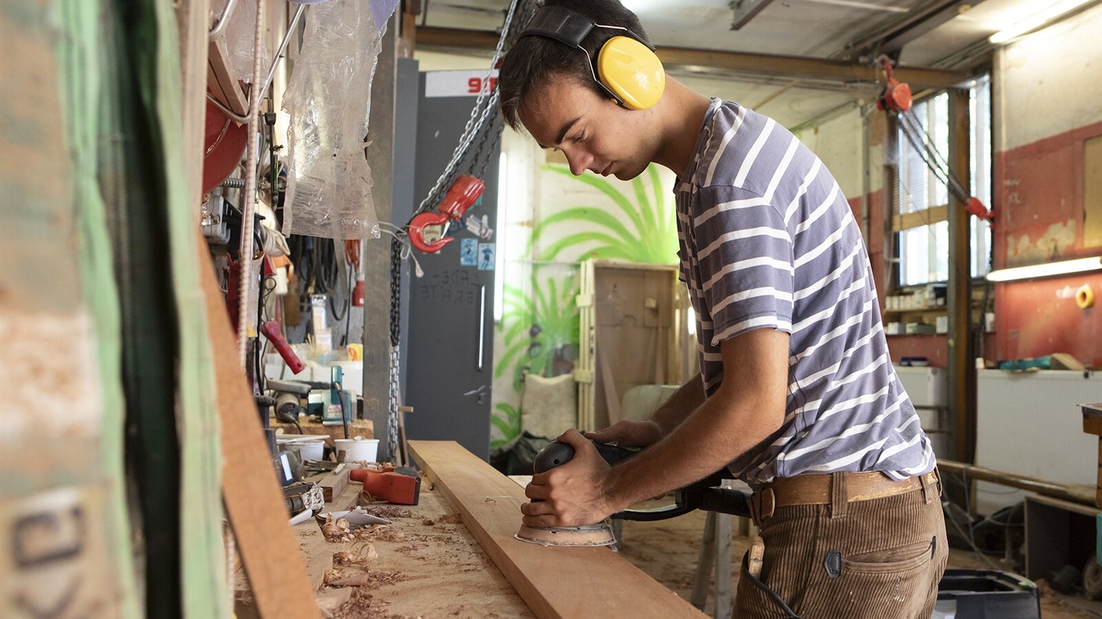 Benedikt schleift ein Holzbrett, aus dem eine Planke angefertigt wird.
