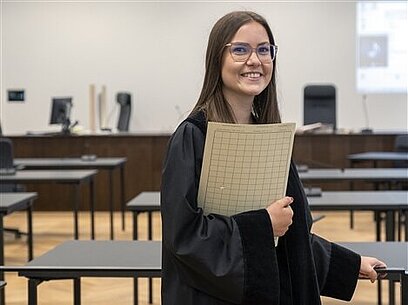 Eine junge Frau in Richterrobe hält eine Akte in der Hand.