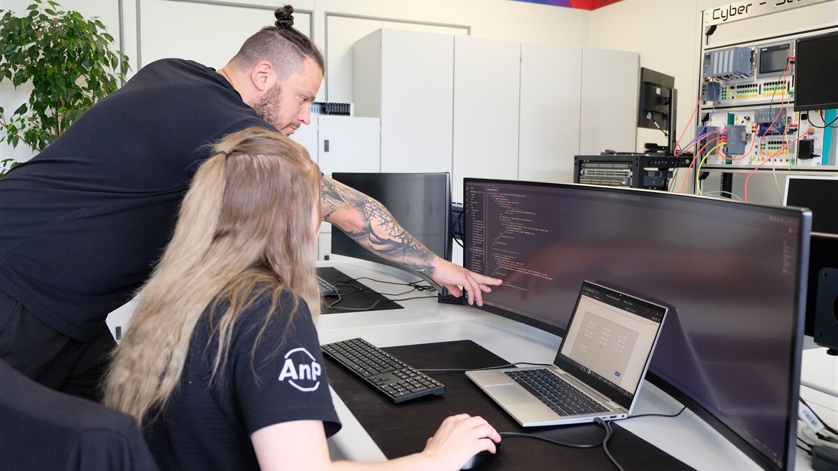 Ayliah sitzt vor dem Computer, während ihr Ausbilder ihr etwas zeigt.