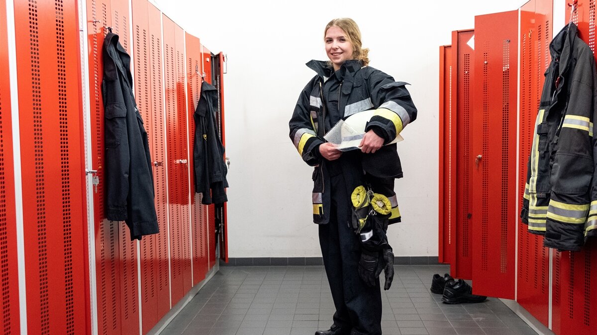 Eine junge Frau trägt eine Feuerwehruniform und einen Helm.