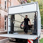 Ein Mann trägt ein dickes Kabel aus einem geöffneten, geparkten Lastwagen.