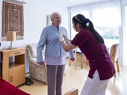 Eine Altenpflegerin hilft einer Seniorin beim Ankleiden.