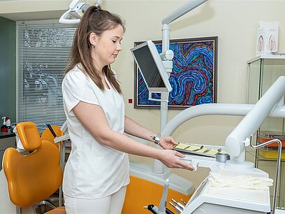 Eine junge Frau in weißer Arbeitskleidung bereitet eine zahnmedizinische Untersuchung vor.