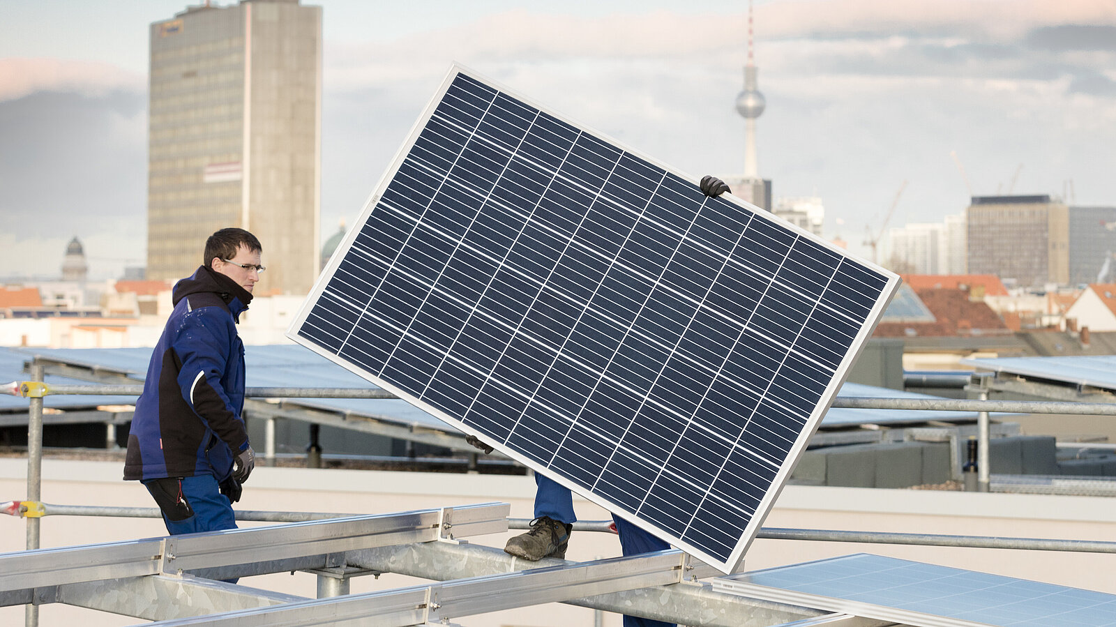 Ein Mann trägt ein Solarpanel auf einem Dach.