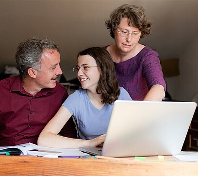 Eine Familie sitzt fröhlich vor einem Laptop.