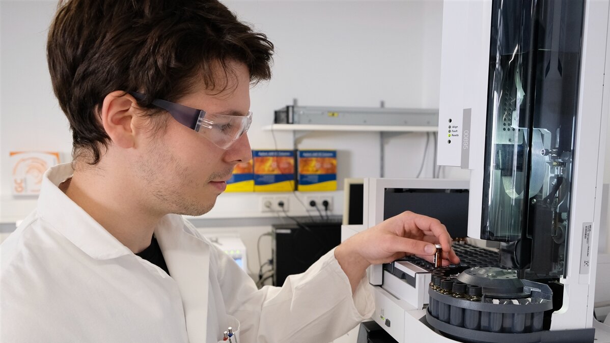 Ein Mann in Laborkittel stellt ein Fläschchen in ein Gerät.