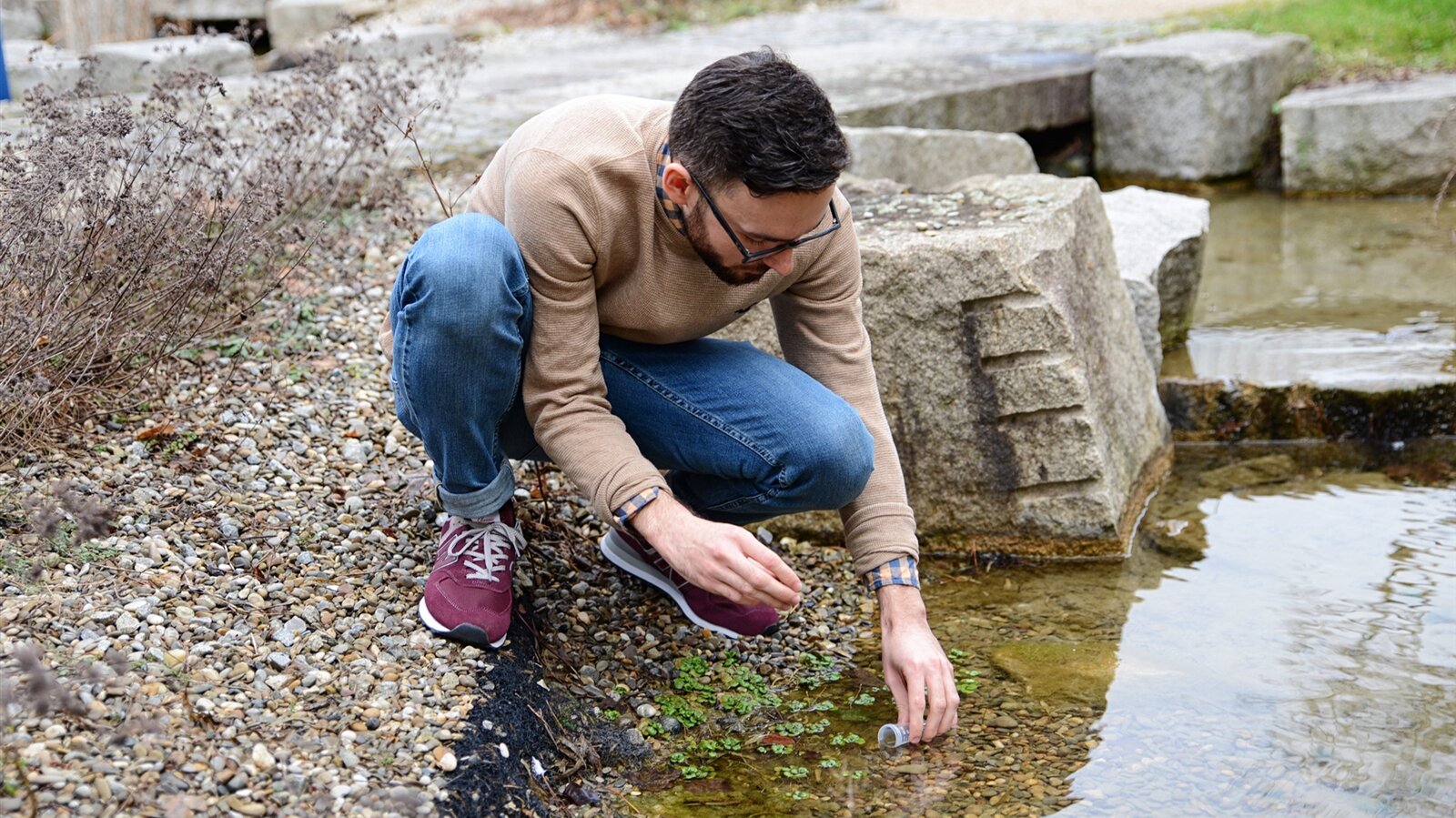 Ein junger Mann entnimmt eine Gewässerprobe aus einem Teich.