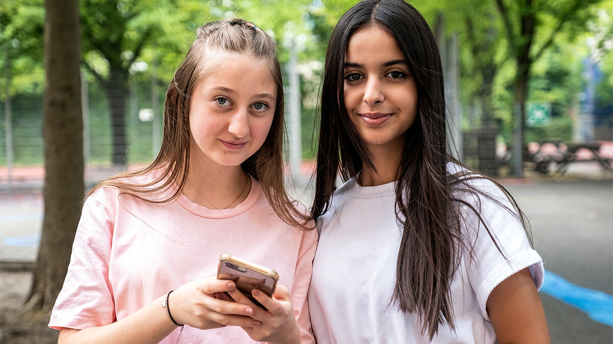 Zwei Schülerinnen schauen von einem Smartphone auf.